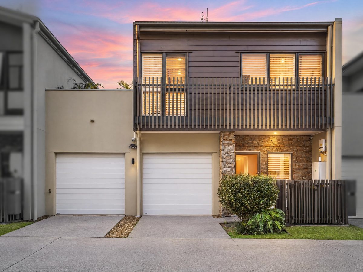 The two-storey townhouse's front at dusk: double garage, stone-clad entry and a slatted balcony