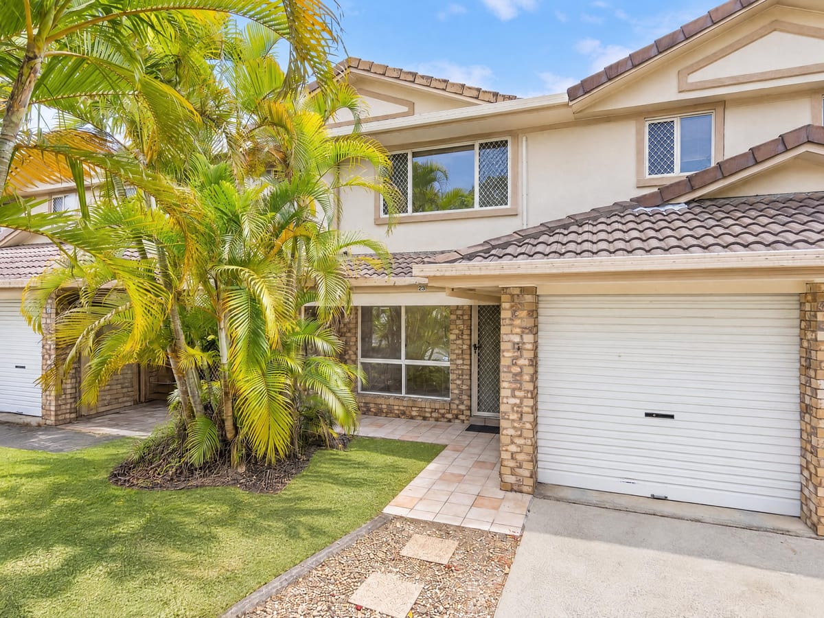 The townhouse's brick-and-render front with its lock-up garage behind a stand of palms
